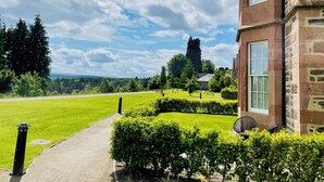 Un bâtiment en pierre avec un chemin pavé menant à une pelouse bien entretenue et offrant une vue sur un paysage lointain.