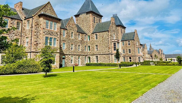 Un grand bâtiment en pierre, doté de nombreuses tours et d’une pelouse bien entretenue.