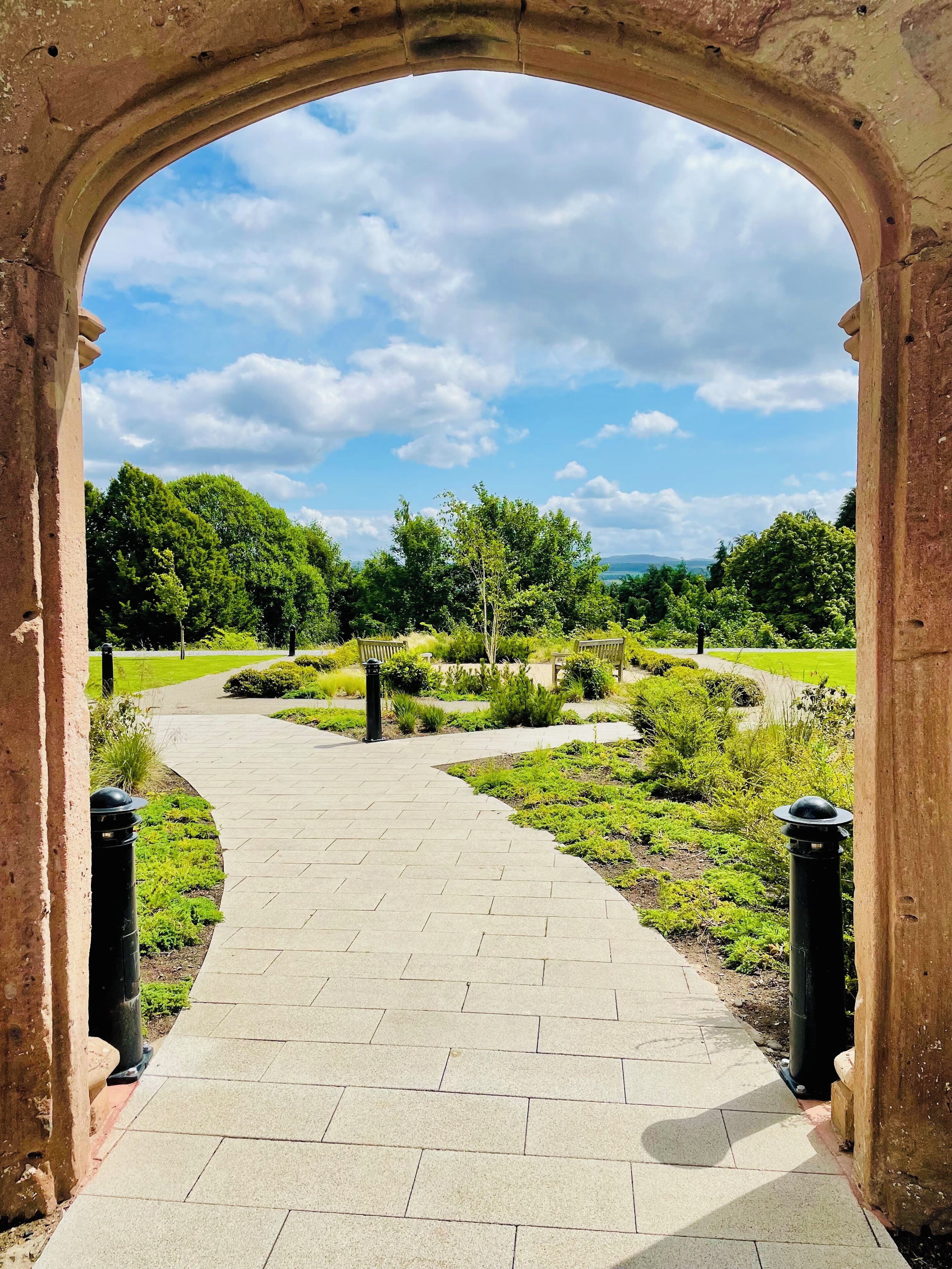 An arched pathway leading through a landscaped garden with a clear sky above.