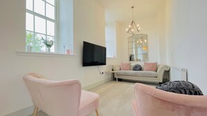 Un salon moderne doté d’une grande fenêtre, d’un téléviseur à écran plat, d’un canapé et de deux fauteuils.