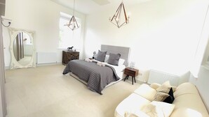Une chambre à coucher moderne avec un grand lit, une table de chevet, une commode, un miroir et un luminaire suspendu.