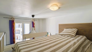 Ein Schlafzimmer mit einem Bett, einem Deckenventilator, einer Nachttischlampe und einem Fenster mit Vorhängen.