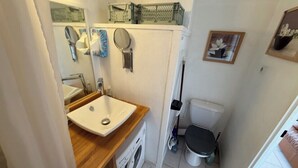 A compact bathroom with a sink, mirror, toilet, and a small washing machine.