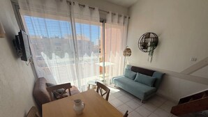 A living room with a wooden dining table, a sofa, and a TV mounted on the wall.