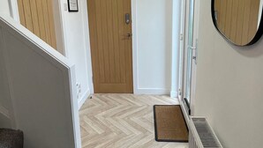 Un couloir avec une porte en bois, un radiateur, un miroir et un parquet à motifs en chevrons.