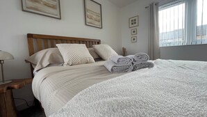Un lit bien fait, avec une couette blanche et des serviettes pliées, une tête de lit en bois et une table de chevet avec une lampe.