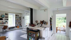 Una habitación amplia con un gran ventanal, una estantería, una zona de cocina y una mesa de comedor.
