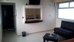 A living room with a sofa, a small table, a TV mounted on a wall, and a window. - Hotel Teocalli Tula (Tula de Allende)