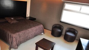 A bedroom with a bed, two chairs, a small table, and a window. - Hotel Teocalli Tula (Tula de Allende)