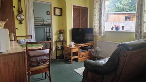 Un espace de vie compact comprenant un lit superposé, un téléviseur, un bureau en bois et un fauteuil en cuir.