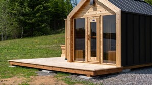 A wooden cabin with a gabled roof, a front door, and a small porch. - Nature’s Channel at Dimensions | Cabin Twelve (Algonquin Highlands)