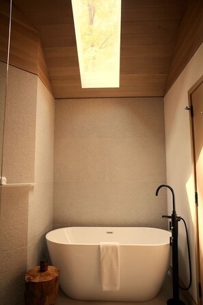A modern bathroom with a freestanding bathtub, a wooden stool, and a skylight. - Nourish + Reset at Dimensions | Cabin Ten (Algonquin Highlands)