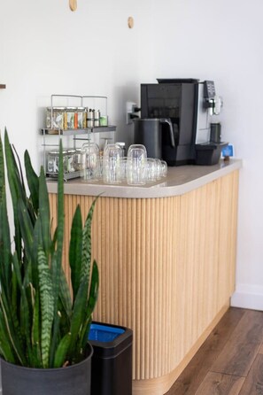 A wooden reception desk with a coffee machine, glassware, and a plant. - Nourish + Reset at Dimensions | Cabin Ten (Algonquin Highlands)