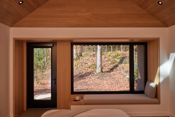 A bedroom with a large window, a bed, and a bench with a cushion. - Nourish + Reset at Dimensions | Cabin Ten (Algonquin Highlands)