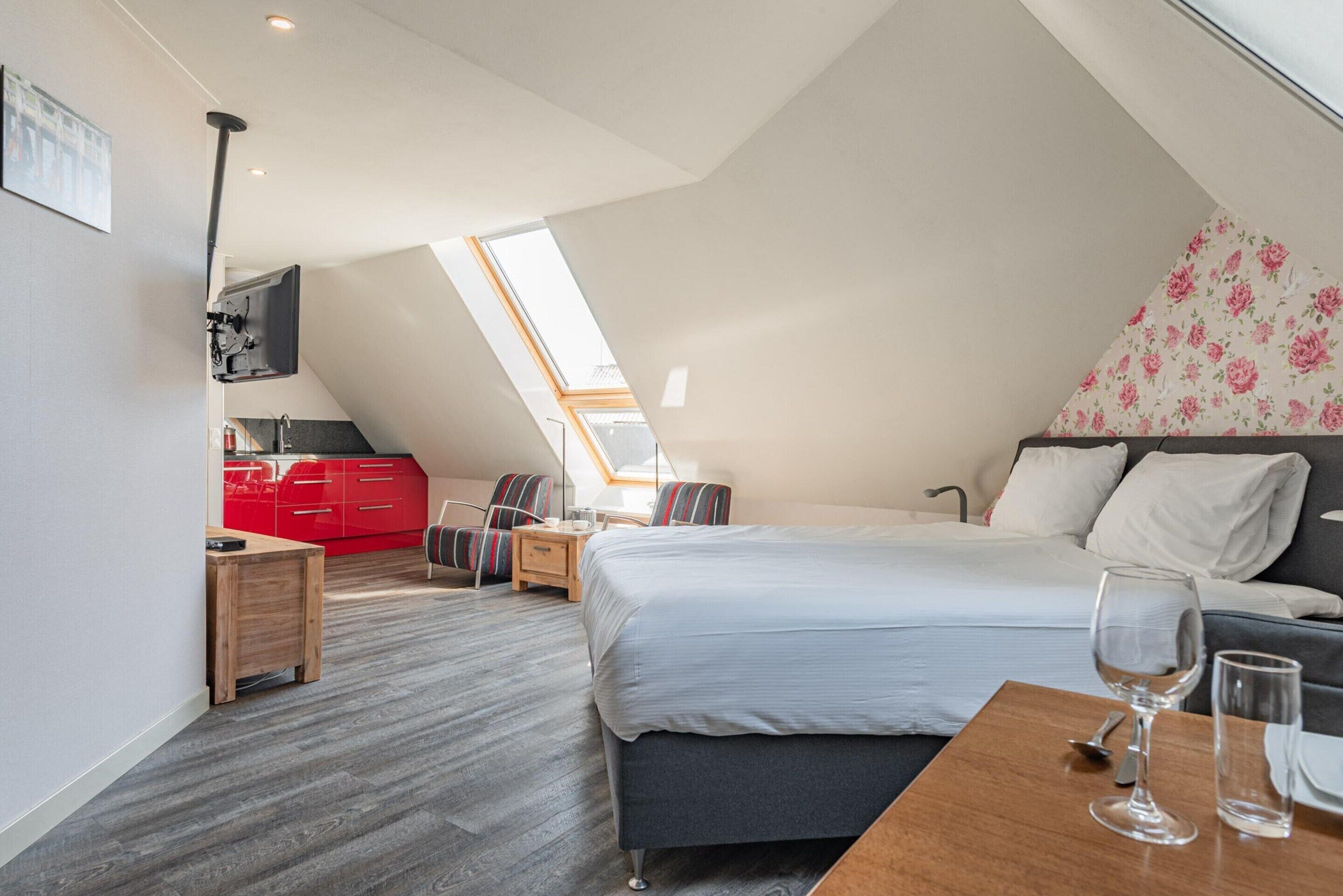 Une chambre moderne avec un grand lit, une table de chevet en bois, un coin cuisine rouge et une lucarne.