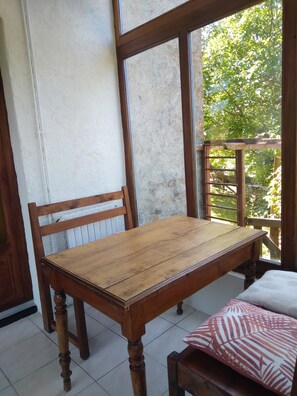 Ein Holztisch mit Stühlen, ein Fenster mit Blick auf Grünflächen und eine weiße Wand.
