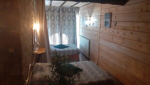 Una habitación pequeña con paredes de madera, una cama con colcha a cuadros, una mesita de noche, una lámpara, una ventana con cortinas y un aplique de pared.