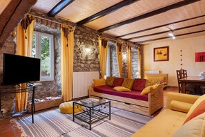 A cozy living room with a stone wall, a sofa, a television, and a dining area.