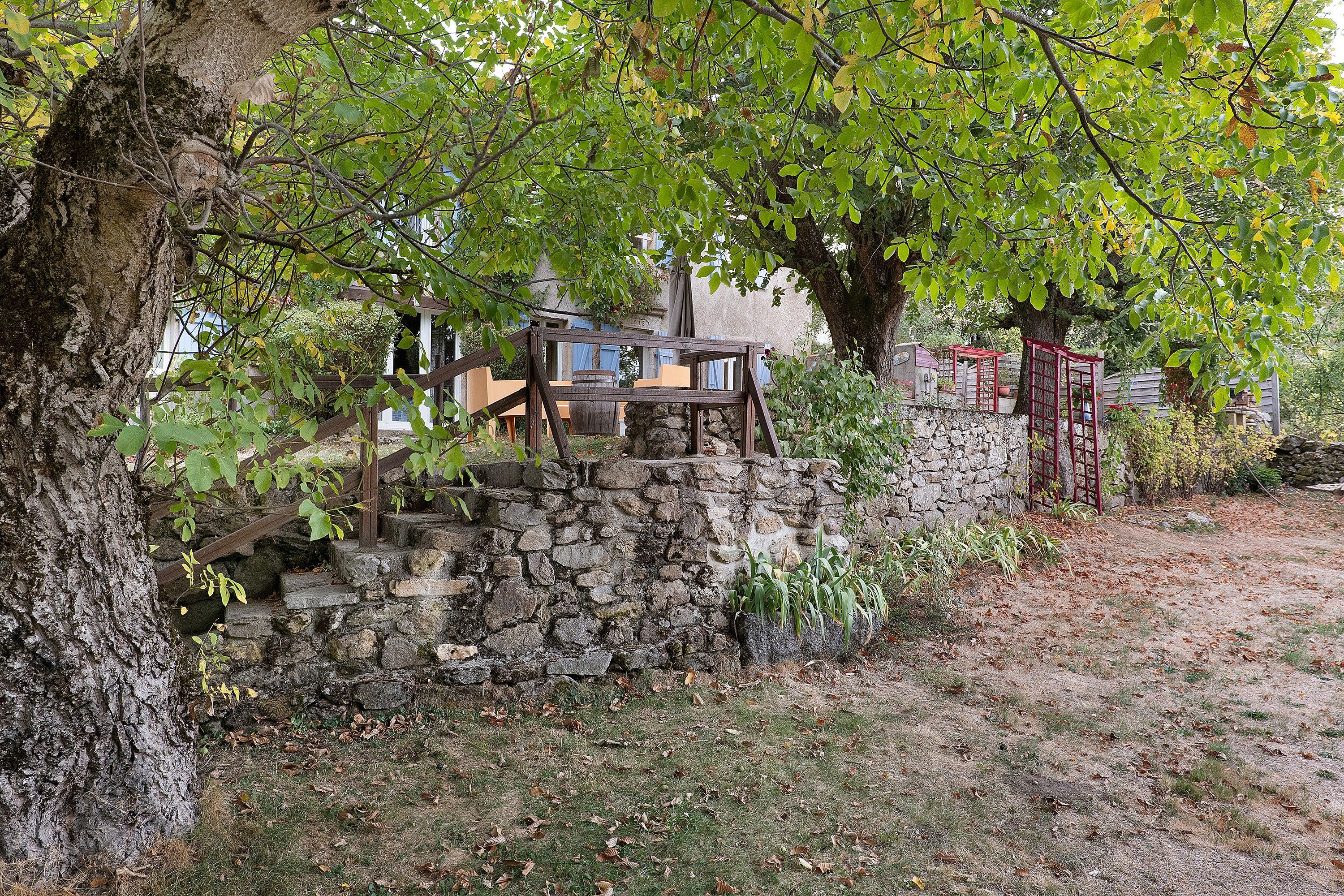 A rustic stone staircase leading up to a wooden deck with a view of a stone wall and trees.