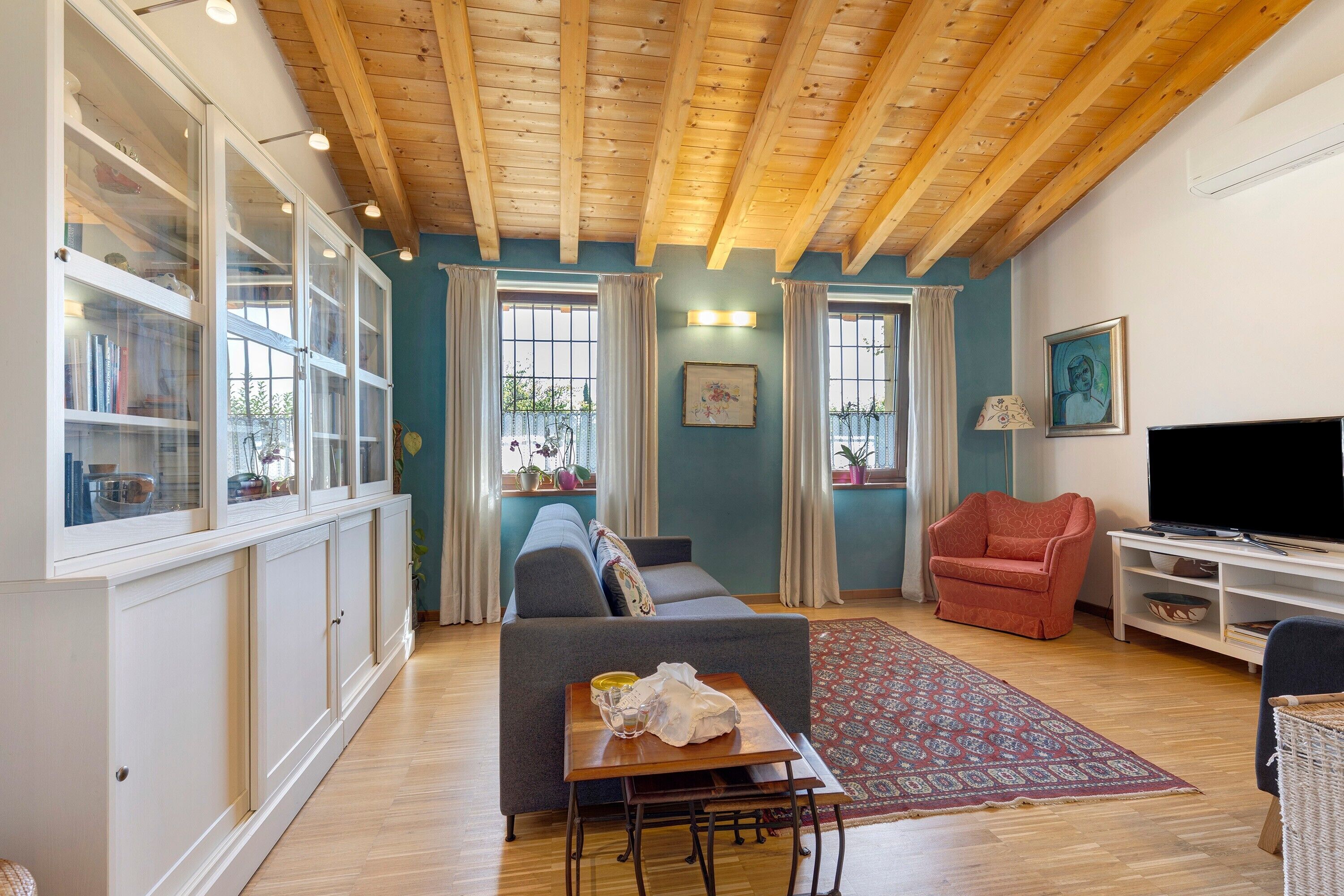 A living room with a sofa, a television, a red armchair, a cabinet with glass doors, and a patterned rug.
