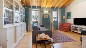Una sala de estar con un sofá, un televisor, un sillón rojo, un aparador con puertas de cristal y una alfombra estampada.
