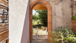 Un arco de ladrillo que da a un jardín con plantas en macetas y una puerta blanca.