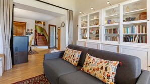 Una sala de estar con un sofá gris, cojines estampados, una estantería y una escalera que lleva a otra habitación.