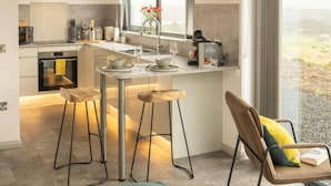 A modern kitchen with a bar area, a TV, and a view of the outdoors. - Migdale Heights - Luxury Cabins in The Highlands (Ardgay)
