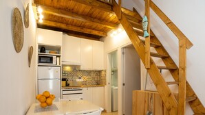 Een compacte keuken met witte kasten, een houten trap en een eethoek met een witte tafel en stoelen.