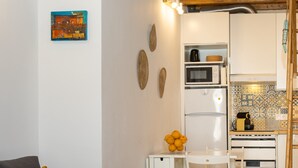 Een knus woongedeelte met een kitchenette, een bank met gele kussens en een kleine eethoek.