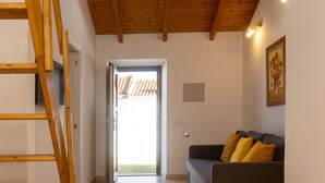 Een kamer met een houten plafond, een dakraam, een trap, een bank met kussens en een deur naar buiten.