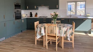 Una cocina moderna con gabinetes verde oscuro, una mesa de comedor de madera y una ventana con vista a un muro de piedra.