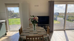 Comedor con mesa preparada para cuatro, un televisor de pantalla plana y vistas a un paisaje rural a través de amplios ventanales.