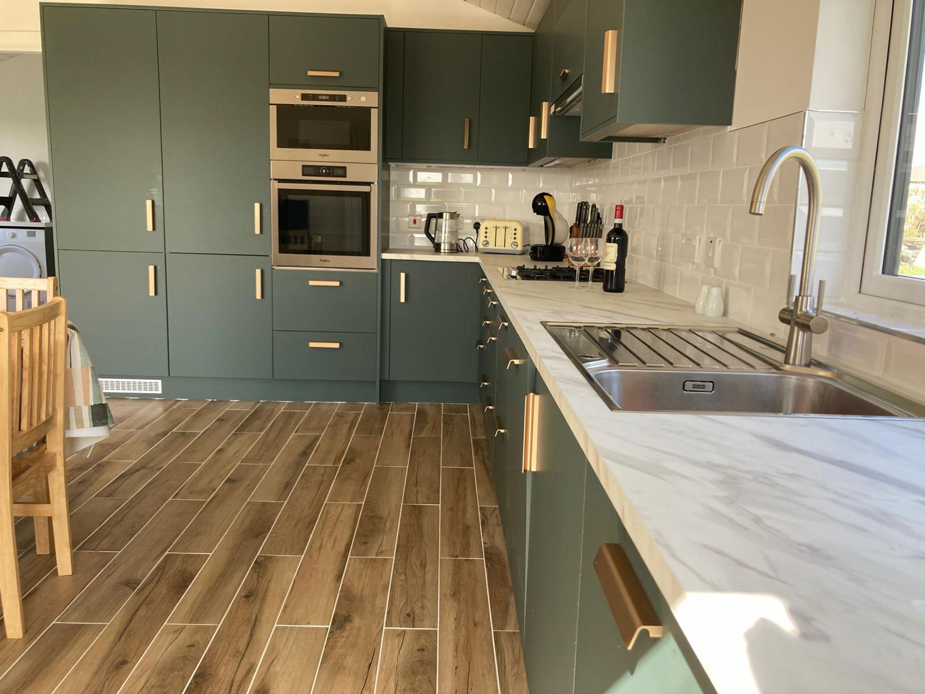 Una cocina moderna con armarios verde azulado, horno empotrado, pileta de acero inoxidable y piso de madera.