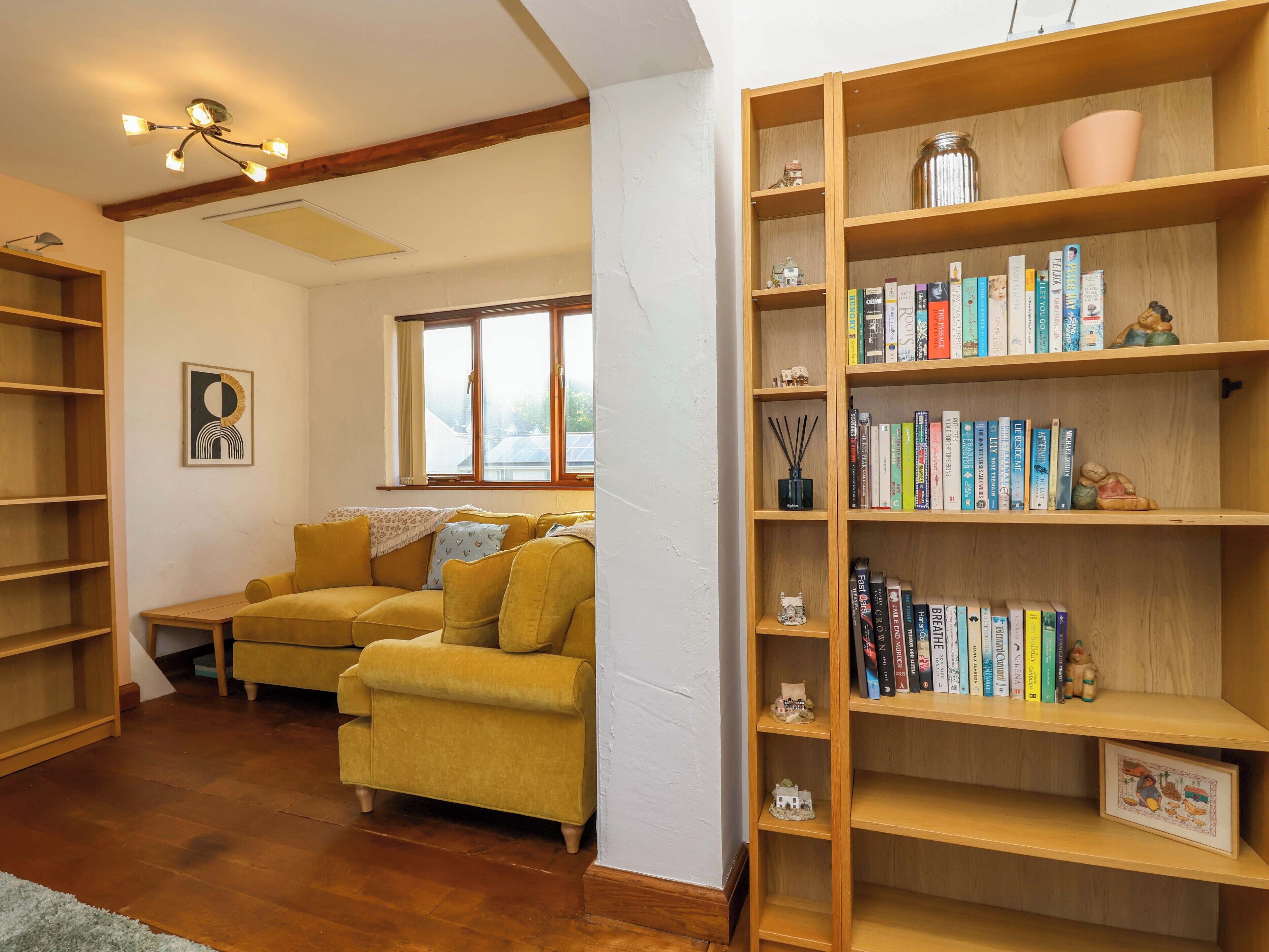 Una sala de estar acogedora con un sofá amarillo, estanterías de madera y un ventanal grande.