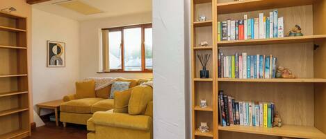 Una sala de estar acogedora con un sofá amarillo, estanterías de madera y un ventanal grande.
