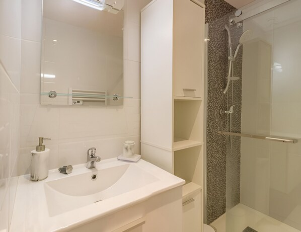 A modern bathroom with a white sink, a mirror, and a glass-enclosed shower.