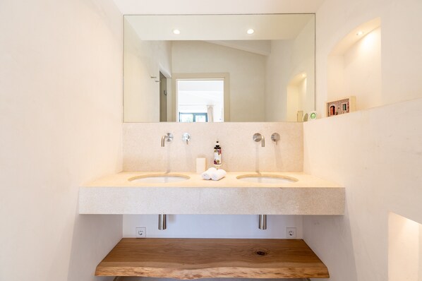 A modern bathroom with two sinks, a large mirror, and a wooden shelf below.