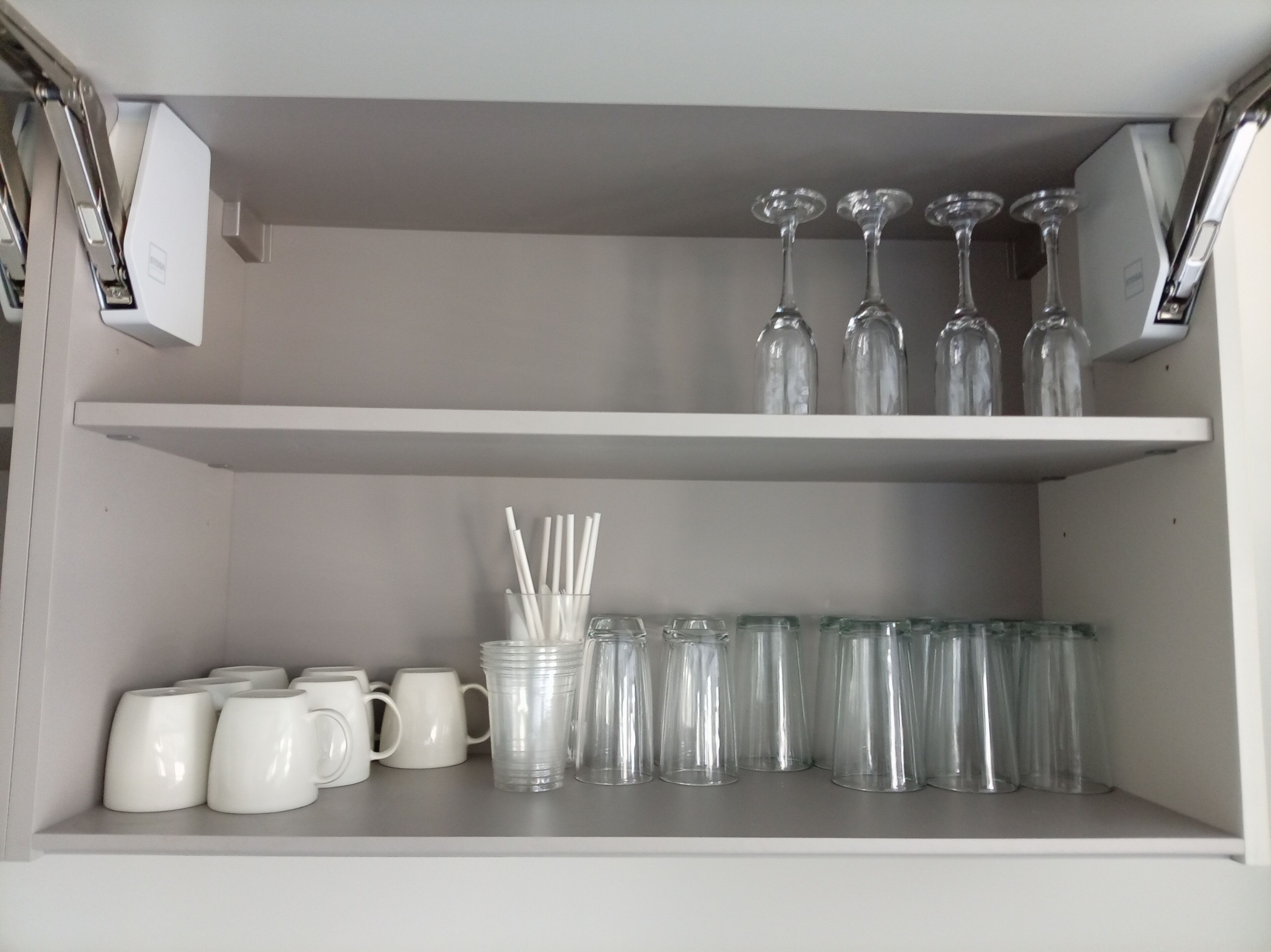 Une étagère de rangement avec des tasses blanches, des verres à boire transparents et un bocal en verre contenant des pailles.