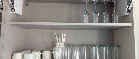 Une étagère de rangement avec des tasses blanches, des verres à boire transparents et un bocal en verre contenant des pailles.