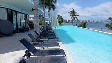Ein Poolbereich mit Liegestühlen, Palmen und Blick aufs Meer.