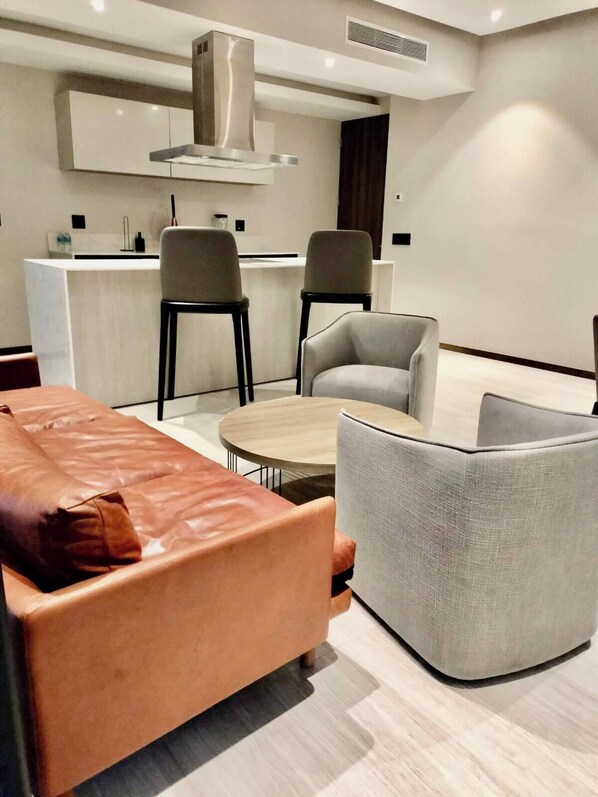 Une cuisine moderne avec un îlot central, deux chaises grises, une table ronde et un canapé marron.