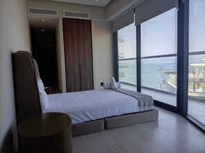 Ein modernes Schlafzimmer mit einem großen Bett, Meerblick und einem Balkon mit Gartenmöbeln.