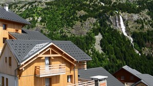 A wooden chalet with a balcony, set against a mountainous backdrop with a waterfall. - View mountain, fitness, swimming pool, hammam, tv, ski locker, 47-52m², Vaujany (Vaujany)
