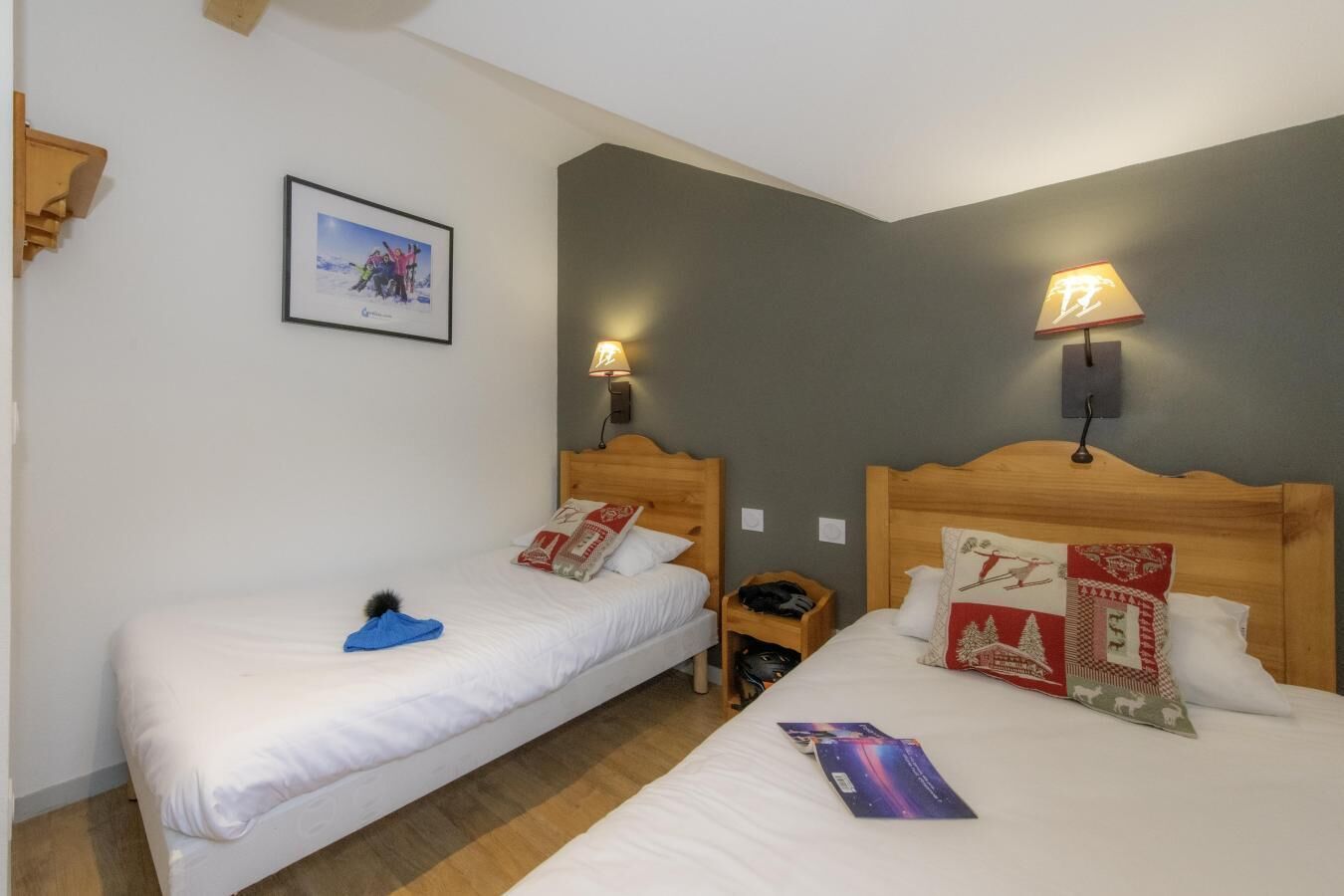 A hotel room with two single beds, a wooden headboard, a nightstand, a lamp, and a framed picture on the wall.
