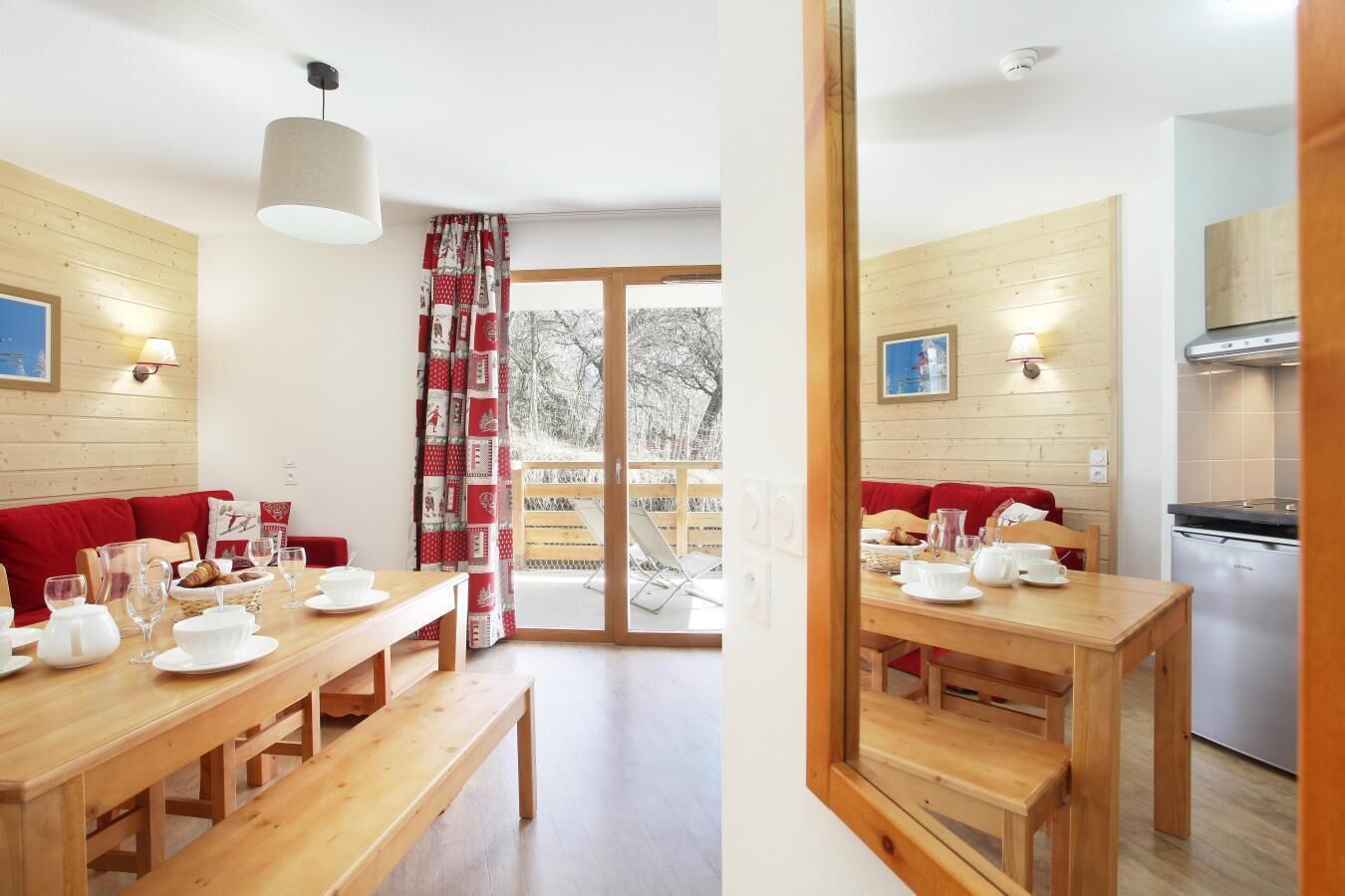 A cozy room with a wooden table set for breakfast, a red sofa, and a view through a glass door to a snowy outdoor area.