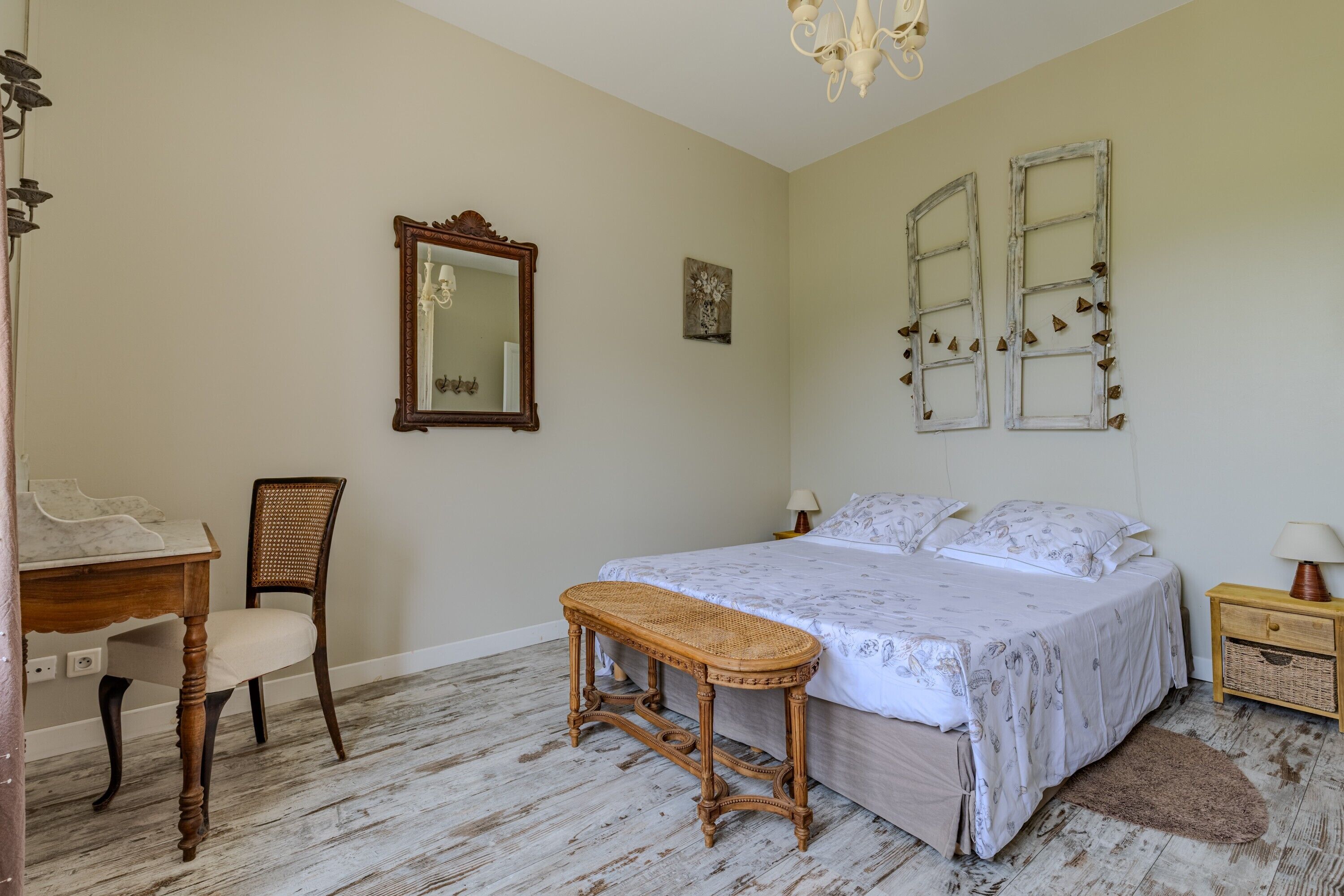 A bedroom with a bed, a chair, a small table, a mirror, and two wall-mounted decorations.