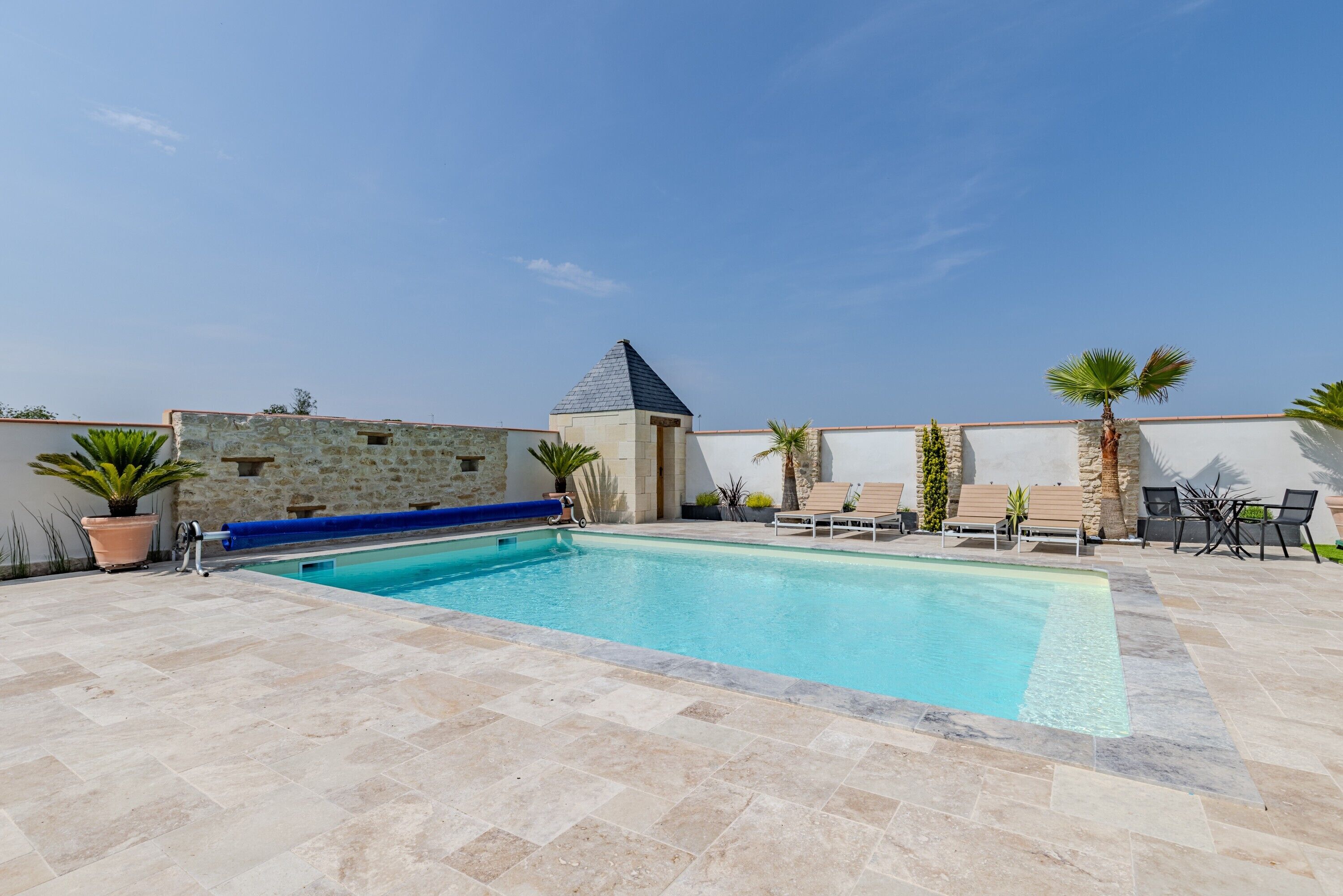 Una piscina con muro de piedra, sillas de descanso y una pequeña estructura tipo torre.