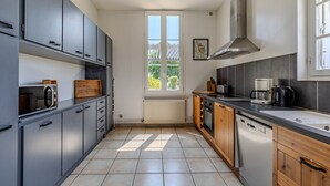 Een moderne keuken met grijze kastjes, een houten aanrechtblad, een inbouwoven en een raam met uitzicht op groen.