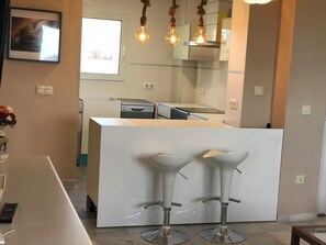 A kitchen with a white island, two bar stools, hanging light fixtures, and a window.